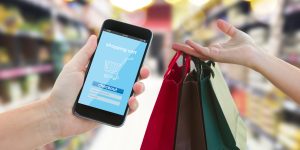 hand holding mobile smart phone with mobile shop  on supermarket blur background and shopping bags - e-commerce concept